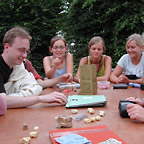 Eine Gruppe Studierender spielt römische Würfelspiele an einem Tisch im Freien.