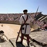 A man in the uniform of a roman gladiator stands at the entrance oft the amphitheater.
